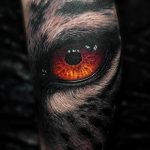 Realistic wolf eye tattoo on forearm, black and grey shading, detailed fur texture, captivating gaze, wildlife tattoo art.