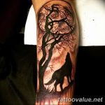 A black silhouette of a howling wolf under a full moon, with a tree in the foreground, on the forearm.