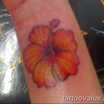 Small, warm-toned hibiscus flower tattoo on the wrist, featuring orange and yellow hues with delicate shading, a subtle and elegant design.