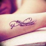 A delicate black ink tattoo on the inner forearm featuring an infinity symbol with a feather, and the word 'life' inscribed within.