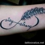 Black and grey forearm tattoo featuring the words 'stay strong' within an infinity symbol, accompanied by a detailed feather, a motivational tattoo design.