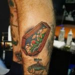 Neo-traditional tattoo of a coffin with a landscape scene inside, featuring mountains and a sun. Placed on the calf, offering a unique visual.