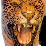 A colorful, realistic tattoo of a jaguar roaring, with detailed fur and facial features, covering a portion of the arm.