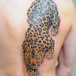 Realistic black and brown jaguar tattoo design on a man's back, showcasing dynamic movement and detailed spot patterns. A striking example of animal tattoo art.