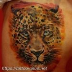 Colorful tattoo of a leopard's face with a fiery orange and yellow palette, showcasing detailed fur and intense eyes.