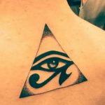 Black ink tattoo of the Eye of Horus within a triangle on the shoulder, representing protection and royal power. A classic Egyptian symbolic tattoo design.