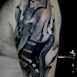 Black and grey tattoo of an electric guitar engulfed in flames on the shoulder, featuring dynamic shading and a powerful visual impact. A striking ink idea.