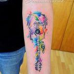 Watercolor style tattoo of an acoustic guitar with musical notes on a forearm, featuring soft colors and flowing lines. A beautiful and artistic tattoo design.