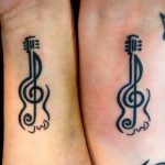 Black ink matching ukulele tattoos on wrists, featuring a stylized design with musical notes, symbolizing harmony.