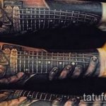 Detailed black and grey realism sleeve tattoo featuring hands gripping a guitar neck, extending down the forearm. Intricate shading and realistic textures.