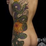 Large Japanese style tattoo of a green snake intertwined with vibrant orange and yellow chrysanthemum flowers, full back piece.