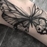 A blackwork butterfly tattoo on the forearm, featuring a detailed, stippled design with delicate linework and a focus on negative space.