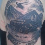 Black and grey memorial tattoo on the upper arm featuring a tank, helicopter, and dates 2014-2015, surrounded by Cyrillic text, honoring fallen soldiers.