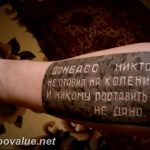 A black and grey text tattoo on the wrist reads a defiant message in Russian, commemorating the resilience of Donbass.