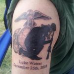 Black and grey silhouette tattoo of the Iwo Jima flag raising memorial, with a name and date, on the upper arm.