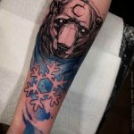 Black and grey bear head tattoo on the forearm, with blue snowflake accents, featuring intricate linework and a wintery aesthetic, a unique tattoo design.