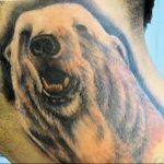 Realistic black and grey tattoo of a grizzly bear's face on a shoulder, showcasing detailed fur texture and a fierce expression.