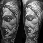 Black and grey realism tattoo of Jesus's face, showing a pained expression. Detailed shading and texture, placed on the forearm.