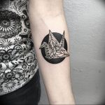 Blackwork tattoo of an origami crane inside a circle with dotwork details, on the inner forearm.