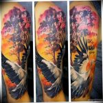A vibrant, full-sleeve tattoo featuring a crane in flight against a backdrop of a fiery forest and sunset, showcasing bold colors and dynamic composition.