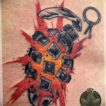 Watercolor style tattoo depicting an exploding grenade with shards and a key, rendered in grey, black, and red splashes.