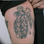 Black and grey tattoo of a grenade with a diamond crown, featuring shading and detail on the thigh.