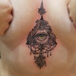 Black ink tattoo of an ornate All-Seeing Eye within a diamond shape, detailed with filigree and teardrop elements, placed on the upper chest.