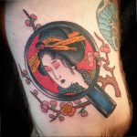 Classic American Traditional style tattoo of a Geisha's face within a circular frame, with cherry blossoms and a sword.