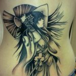 Black ink tattoo of a geisha with wings on a torso, featuring a fan and floral elements in a dynamic composition.