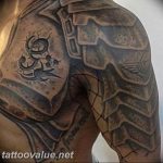 Black and grey Spartan helmet tattoo on the shoulder, featuring tribal elements and script, with a rough, textured aesthetic.