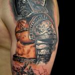Realistic black and grey gladiator tattoo on the shoulder and upper arm, featuring a helmet, muscular torso, and a battle scene. Detailed shading and dynamic composition.