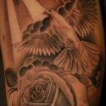 Black and grey tattoo of a dove flying amidst clouds and rays of light, with a rose below, on a forearm. Realistic style.