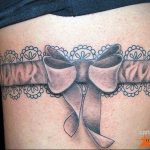 A black and grey tattoo of a lace garter with a bow, wrapping around the thigh, showcasing intricate detailing and a vintage aesthetic.