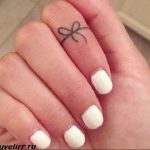 Tiny black outline bow tattoo on the side of a finger, showcasing a minimalist style. A delicate and discreet tattoo design for a subtle look.