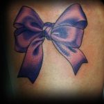 A beautiful purple bow tattoo with subtle shading, creating a silky texture. This tattoo is placed on the shoulder, offering a graceful and feminine aesthetic.