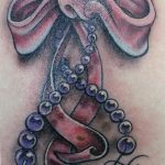 Detailed pink bow with pearl strand tattoo on the chest, showcasing realistic shading and a classic, elegant style.