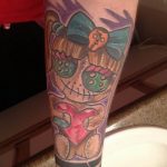Neo-traditional voodoo doll tattoo sleeve with a bow, heart, and stitched details, in purple, teal, and pink hues.