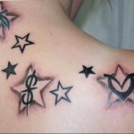 Unique tattoo featuring a collection of stars with various symbols inside (dollar sign, heart, yin yang) on the shoulder, a personalized and eclectic design.