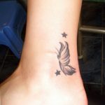 Small black and grey tattoo on the ankle featuring a bird's wing with stars, symbolizing freedom and dreams. A feminine and subtle tattoo art piece.