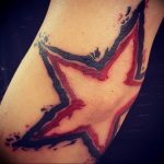 Abstract tattoo of a star with red and black ink and splatter effects on the forearm. Minimalist design with a bold and edgy style.