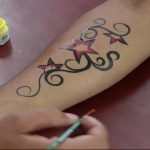 Red and black star tattoo on the forearm, with swirling henna-like patterns, a vibrant and artistic design.