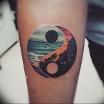 Colorful tattoo of a Yin Yang symbol depicting a seascape and a forest landscape, a vibrant and detailed design on a forearm.