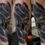 Detailed black and grey biomechanical tattoo on a calf, depicting exposed gears, pistons, and metallic structures. Realistic shading and a dynamic composition.