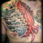 Colorful tattoo on the shoulder and chest featuring a biomechanical design with swirling patterns and vibrant red and blue hues. A unique and artistic tattoo design.