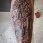 Detailed biomechanical tattoo on a calf, featuring metallic components, gears, and pistons in black and grey, creating a realistic effect.