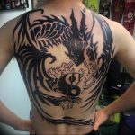 Full back tattoo featuring a large yin yang symbol surrounded by tribal patterns and a stylized dragon, in a bold blackwork style.