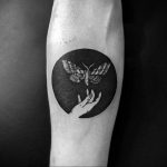 Blackwork tattoo featuring a moth resting on a hand within a circular frame on the forearm, a mystical and symbolic design.