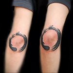 Black ink Enso circle tattoos on both knees, featuring a brushstroke style. The minimalist design embodies Zen Buddhist principles of simplicity and enlightenment.