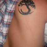 Black ink Tree of Life tattoo on the upper shoulder, featuring flowing lines and a minimalist style. A popular choice for symbolic ink ideas.
