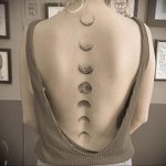 Black ink tattoo of a series of moon phases running down a woman's spine, minimalist style, celestial design.